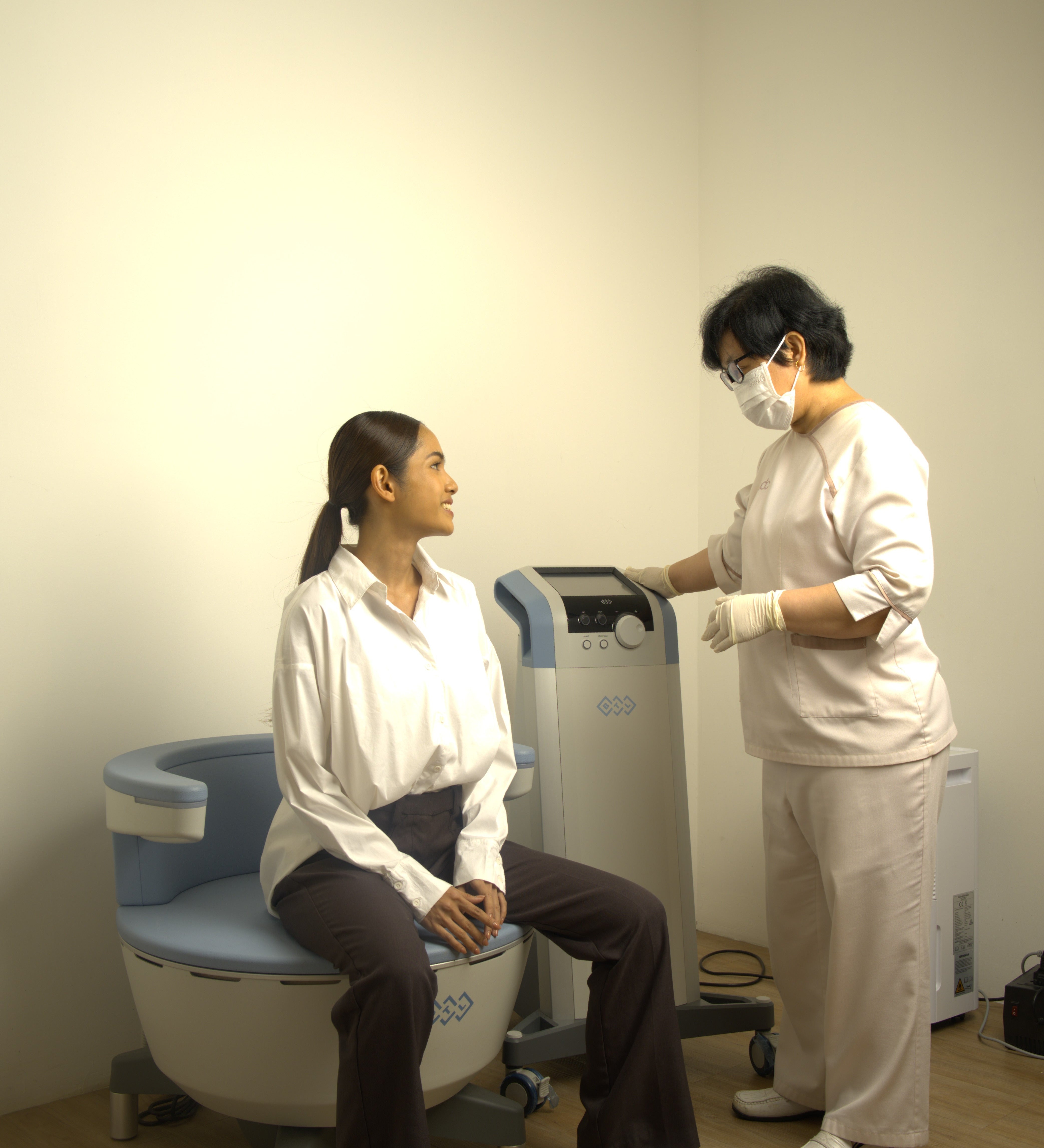 Two individuals in a medical or clinical setting with a machine on a white background