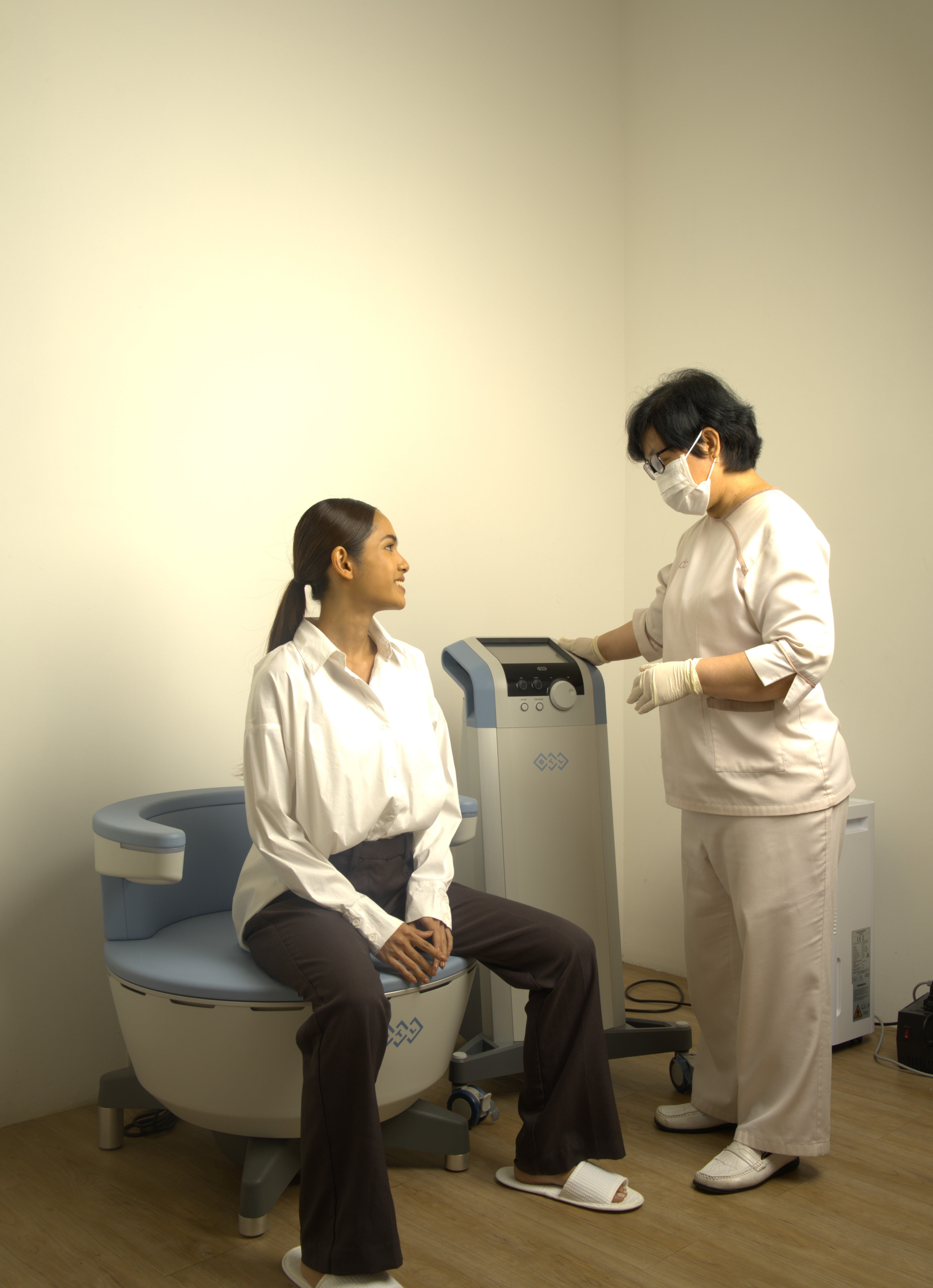 Two individuals in a medical or clinical setting with a machine on a white background