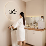 Woman in a white robe standing on a scale in a modern bathroom with 'adc' branding.