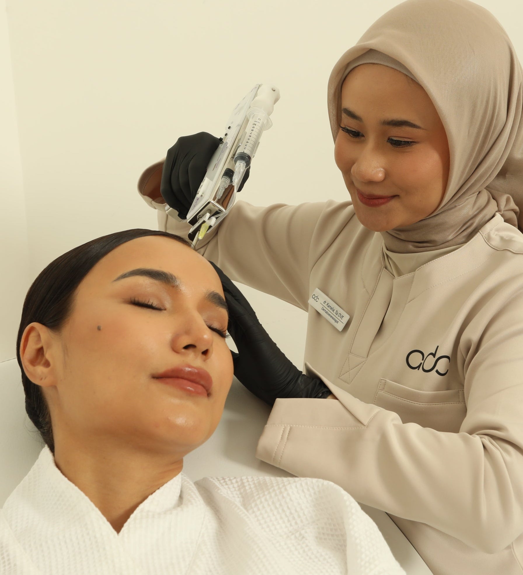 A woman receiving a Premium Hair Growth treatment from another woman in a beige hijab against a plain background