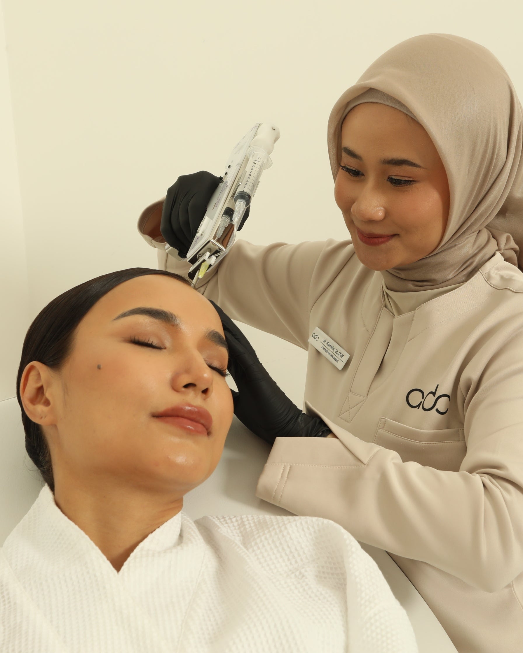 A woman receiving a Premium Hair Growth treatment from another woman in a beige hijab against a plain background